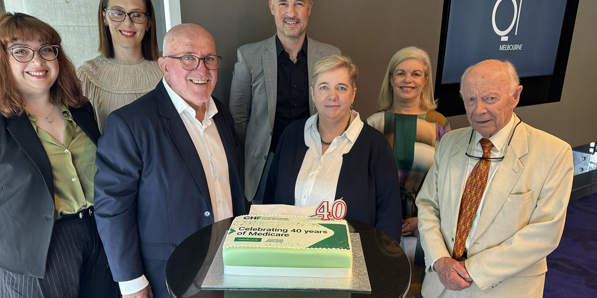 A gourp of people standing around a cake celebrating Medicare's 40th anniversary